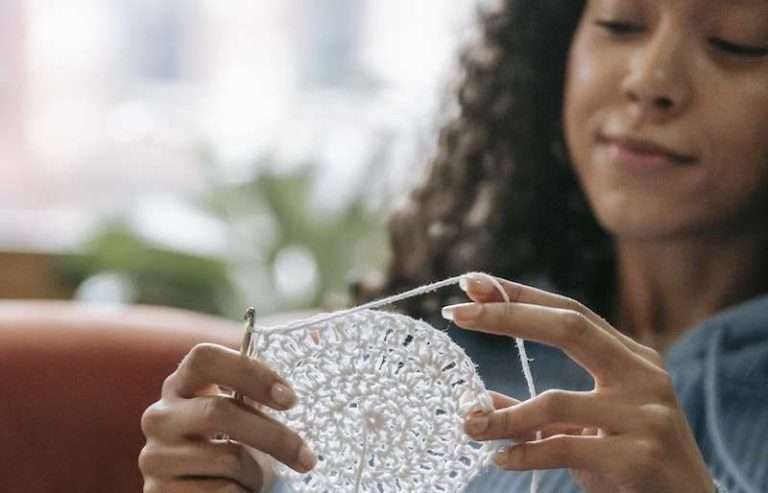A Woman Holding a White Crochet Thread and a work in progress doily